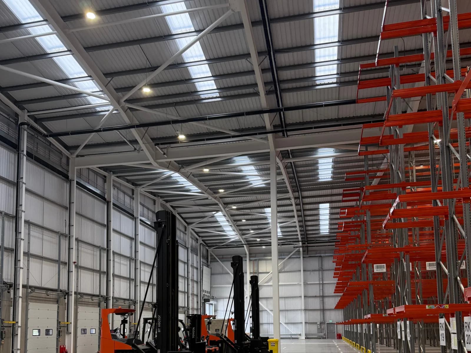 Steel portal frame, rafters and bracing inside a completed industrial unit, with cantilever racking installed